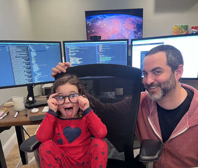 Justin at his desk with his daughter making a face in his chair